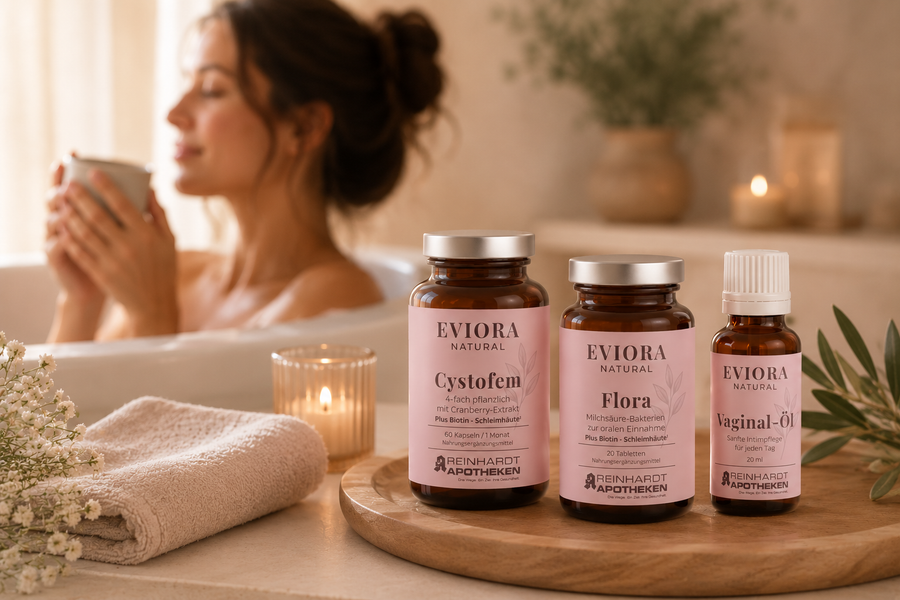 EVIORA Natural Produkte Cystofem, Flora und Vaginal-Öl arrangiert auf einem Holztablett in warmer Spa-Atmosphäre mit entspannter Frau im unscharfen Hintergrund – Premium-Selfcare und Intimpflege zuhause.