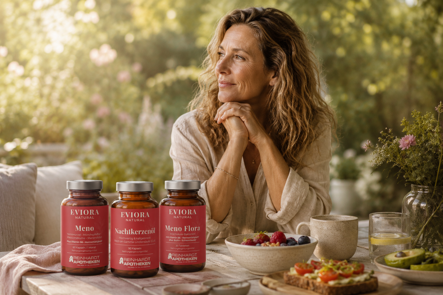 Entspannte Frau Mitte 40 genießt ein gesundes Frühstück im sommerlichen Garten bei warmem Morgenlicht. Im Vordergrund stehen die EVIORA Produkte Meno, Nachtkerzenöl und Meno Flora in natürlicher Wellness-Atmosphäre.