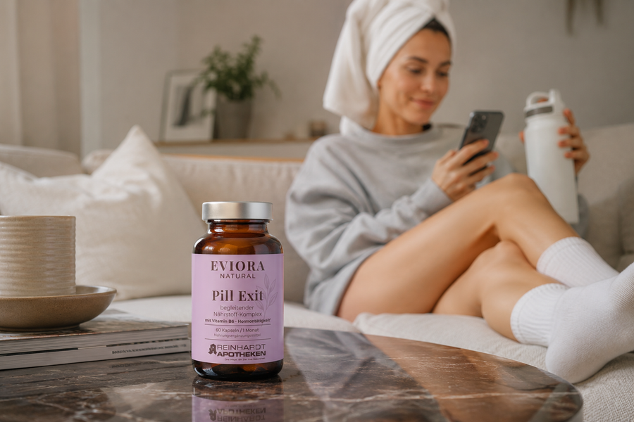 Junge Frau im Oversize-Pullover mit Handtuch um die Haare sitzt entspannt auf dem Sofa mit großer Wasserflasche und Smartphone. Im Vordergrund steht das EVIORA Pill Exit Produkt auf dem Couchtisch in ruhiger Female-Health-Lifestyle-Atmosphäre.